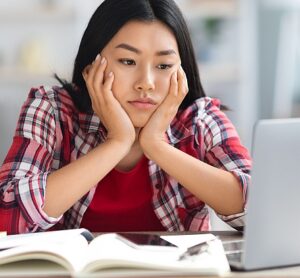 Online Education Problems. Tired Young Asian Student Lady Looking At Computer Screen, Bored Korean Woman Sitting At Desk With Computer, Having Difficulties With Distance Learning, Free Space